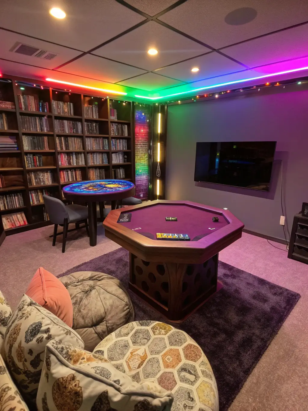 Colorful basement gaming room with hexagonal table, game-filled shelves, galaxy print beanbag chairs, and neon game controller sign.
